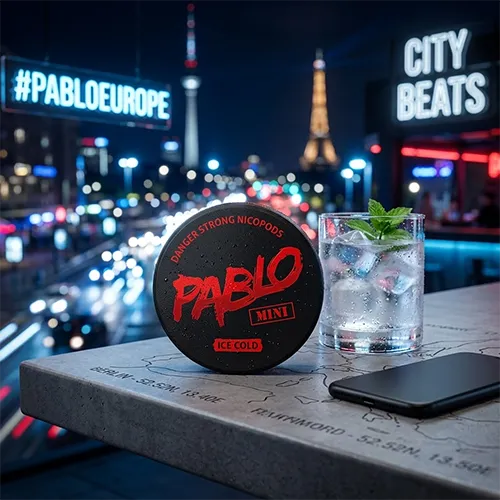 PABLO Mini Ice Cold nicotine pouches tin on a city balcony overlooking Europe at night